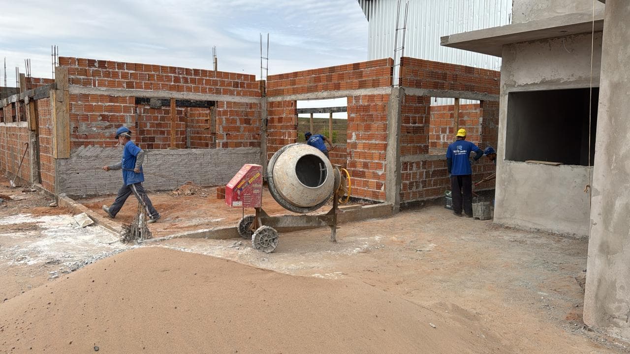 Paredes em alvenaria de tijolo sendo levantadas por equipe própria, com caminhão-betoneira em obra